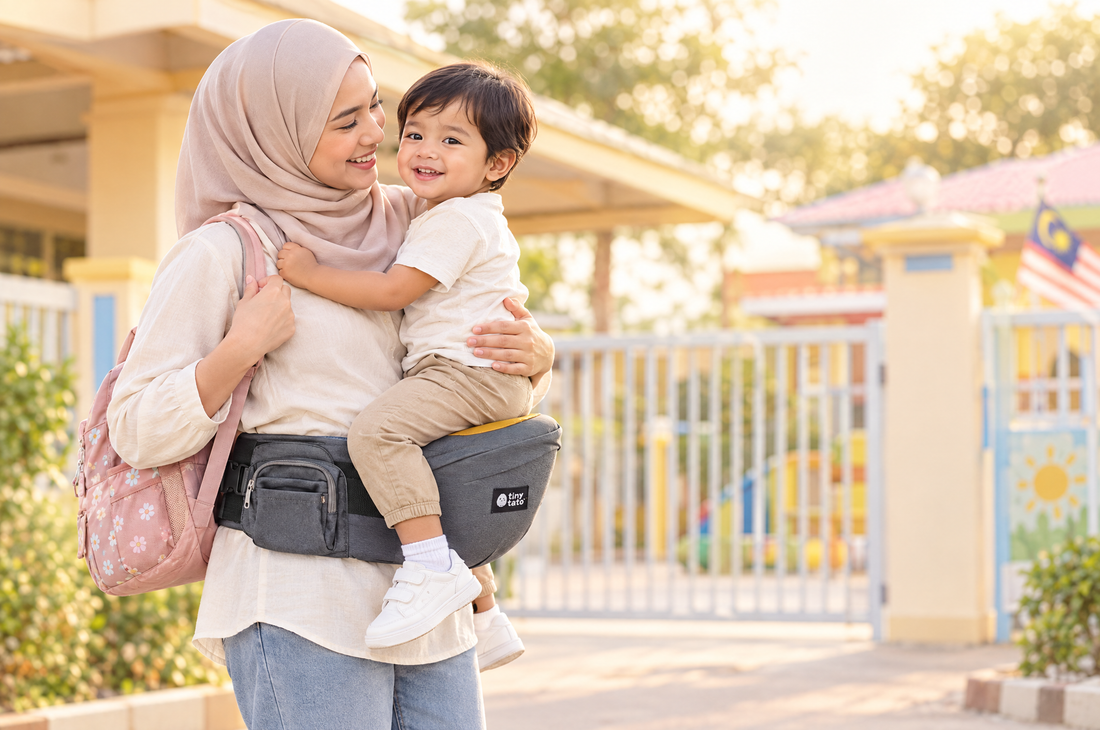 Mum at a kindergarten gate carrying a 2-year-old on a TatoHip hip seat carrier with one arm around the child