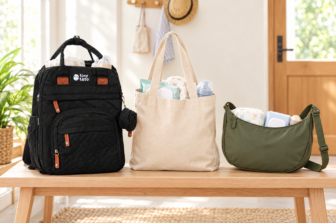 Black TatoNest diaper backpack next to a canvas tote bag and an olive sling bag on a bench, comparing diaper bag types