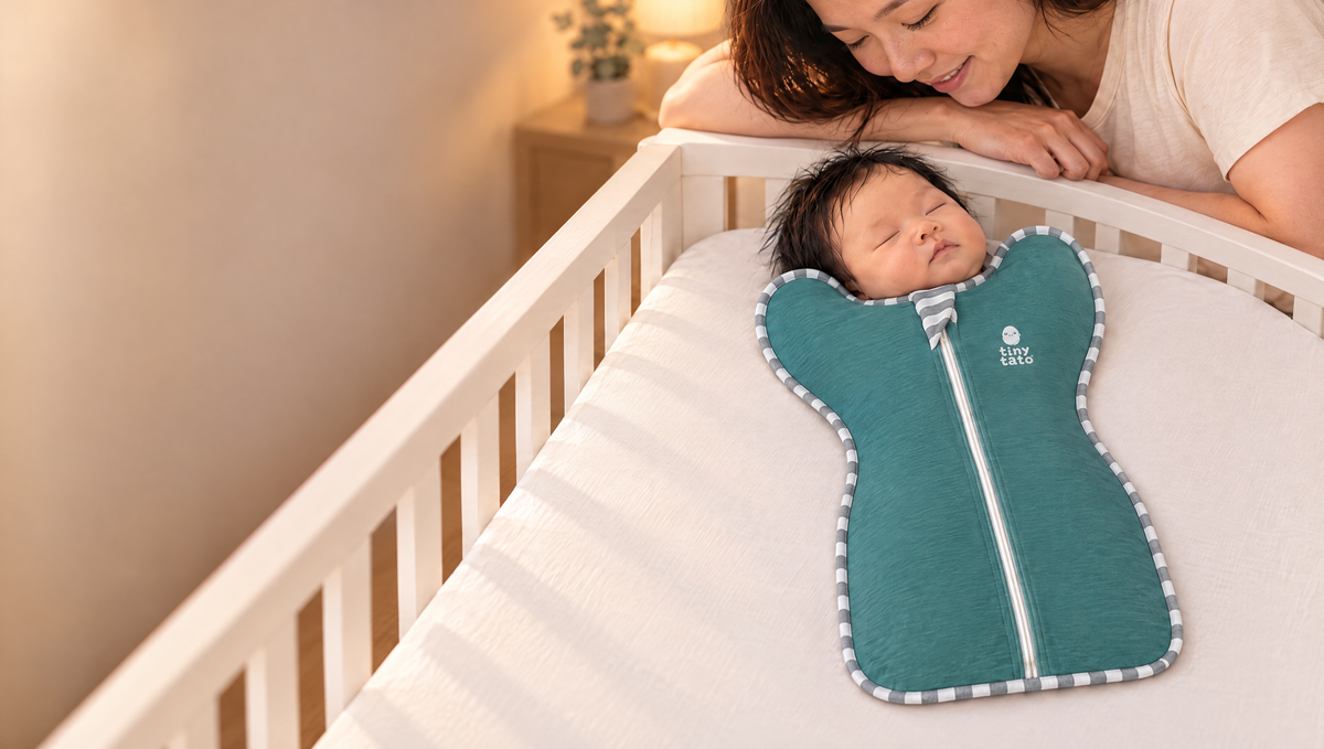 Mum smiling over her newborn asleep in an Ocean Mist TatoWrap zip swaddle in a cot