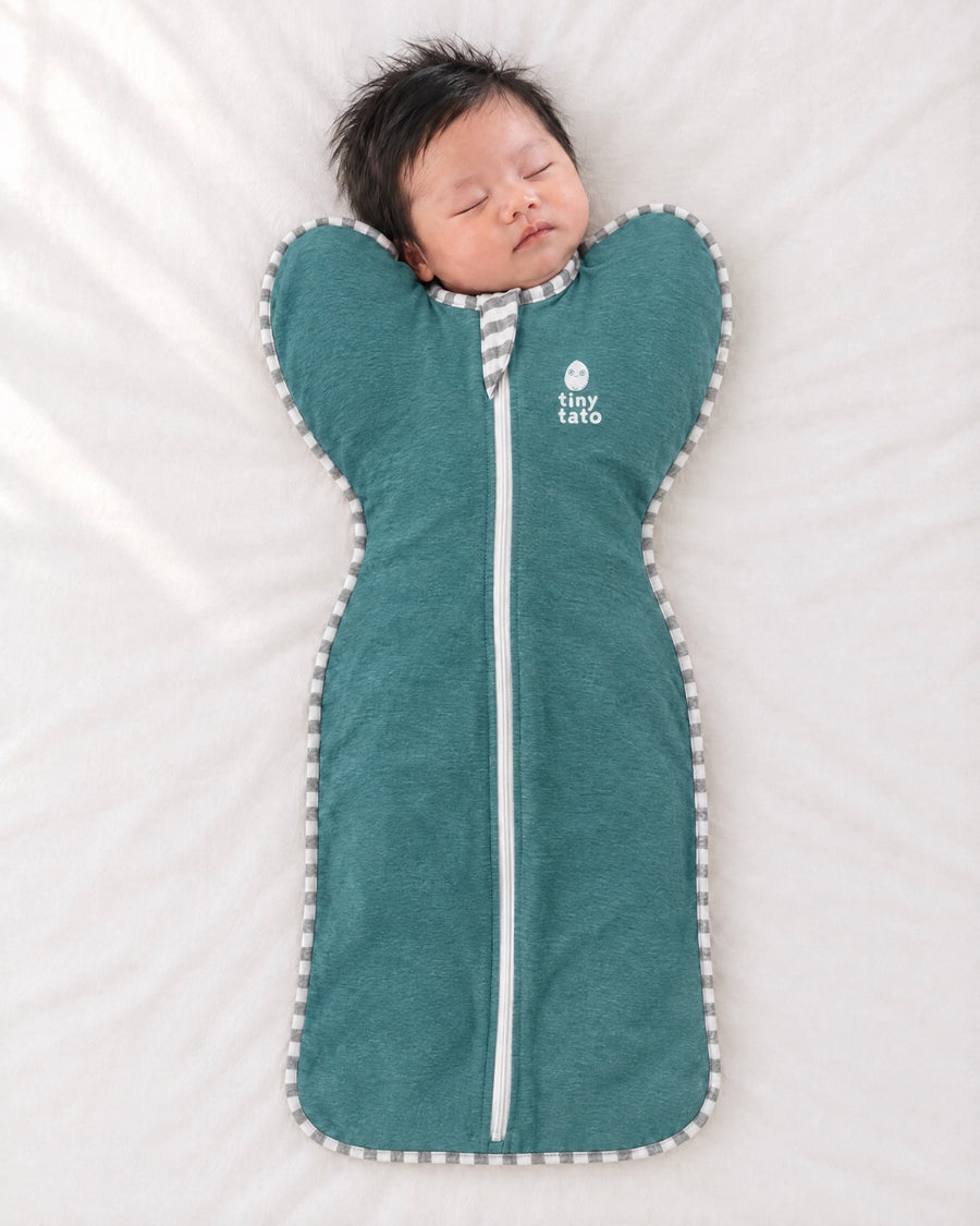 Newborn asleep on their back in an Ocean Mist TatoWrap swaddle with arms up